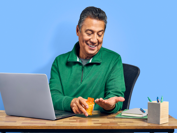 man sits at a desk in front of a computer and takes medication
